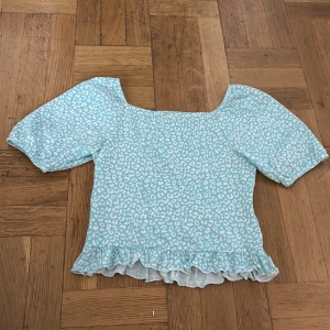 Blå leopardmönstrad blus KappAhl - Supersöt blus från KappAhl i ljusblått med vitt leopardmönster. Modellen har korta puffärmar, fyrkantig halsringning och smockad panel på ryggen. Volangkant nedtill ger en extra girly vibe. Perfekt för dig som gillar att sticka ut med färg och mönster.