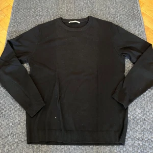 Svart stickad tröja från A Day's March - Svart stickad tröja från A Day's March i storlek M. Klassisk rund hals och ribbade muddar vid ärmslut och nederkant. Enkel och stilren design som funkar till många olika looks. Perfekt för dig som gillar minimalistiskt och cleant.