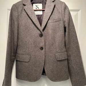 Ullkavaj Dam Gant & Sons strl 36 - Supersnygg ullkavaj från Gant. Grå/brun med beige lappar på armbågarna, ingen slits bak. Lätt figursydd, läckert till ett par jeans. Mycket fint skick. Strl 36