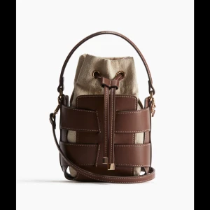 Brun och beige bucket väska från hm! - Trendig HM bucket väska!! Super snygg, de enda defekterna är att en liten bit läder har gått av vid kanterna!!
