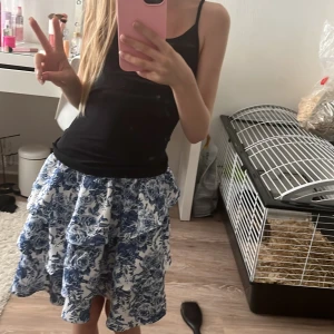 Blommig volangkjol i blått och vitt - Supersöt kjol med blått och vitt blommönster, volanger och elastisk midja. Kjolen är knälång och har en luftig känsla, perfekt för varma dagar. Materialet är 100% polyester och tyget är mjukt och följsamt. Säljer den för att tycker den e för lång för min smak!❤️ den e ganska stor så den hade kunnat passa en 12 åring till och med❤️