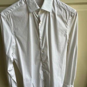 Vit skjorta från Massimo Dutti - Klassisk vit skjorta från Massimo Dutti med italienskt tyg. Skjortan har lång ärm, knappar framtill och stilren krage. Perfekt för dig som gillar en clean och tidlös look. Materialet är mjukt och känns lyxigt mot huden.