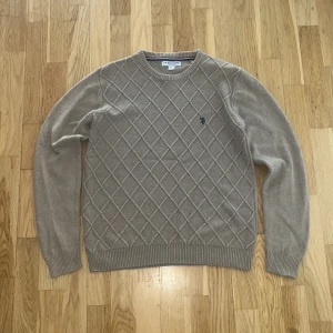 Beige rutig stickad tröja U.S. Polo Assn storlek M. - Snygg beige stickad tröja från U.S. Polo Assn. med rutigt mönster över hela framsidan och broderad logga på bröstet. Rund hals och ribbade muddar vid ärmslut och nederkant. Perfekt för dig som gillar klassisk stil med en twist. Storleken är M och tröjan är i mycket bra skick. Har du några funderingar kom skriv dm.