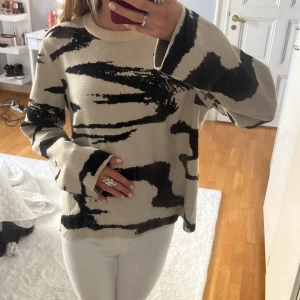 Beige och svart stickad tröja - Säljer en beige stickad tröja med svart abstrakt mönster. Tröjan har rund halsringning och långa ärmar med lite loose passform. Perfekt för dig som gillar coola prints och vill ha en unik look. Passar till både jeans och kjol.