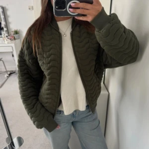 Olivgrön quiltad bomberjacka Zara - Säljer en olivgrön quiltad bomberjacka från Zara med vågigt mönster och ribbade muddar. Jackan har dragkedja framtill och är långärmad med loose passform. Perfekt för dig som gillar streetstyle och vill ha en unik jacka i garderoben.