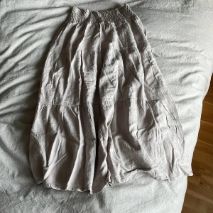 Beige långkjol från lager 157 - Säljer en beige långkjol från lager 157 med smock i midjan och ett luftigt, böljande tyg. Kjolen har flera sömmar som ger en cool, avslappnad look och är perfekt för dig som gillar enkel och stilren design.