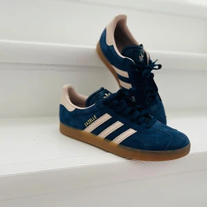 Adidas Gazelle blå sneakers strl 38 2/3 - Säljer ett par Adidas Gazelle sneakers i marinblå och rosa ränder. Knappt använda- kanske 1-2ggr. Säljer då jag beställde online och dom var för små. 