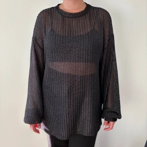 Svart ribbad metallic meshtröja med lång ärm - Säljer en svart, transparent metallic/glittrig meshtröja med ribbad struktur och lång ärm. Tröjan har en loose passform och rund halsringning, perfekt för att styla lager på lager. Materialet är lätt och luftigt, vilket gör den riktigt skön och edgy.