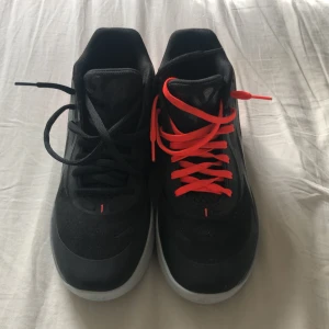 Puma MB.01 sneakers svart/röd 40.5 Basketskor - Säljer ett par Puma MB.01 sneakers i svart med röda detaljer och cool grafik på hälen. Ena skon har svarta snören och den andra röda, vilket ger en unik look. Skorna har en låg profil och är tillverkade i syntetmaterial med textilfoder och platt sula.