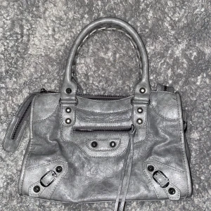 Grå skinnhandväska med detaljer - cool väska med nitar. dragkedjan har gått sönder men funkar att stänga som vanligt 