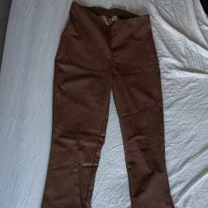 Bruna bootcut byxor i skinnimitation - Snygga bruna byxor från H&M Divided i skinnimitation. Modellen är bootcut med medel midja. Perfekta för dig som vill ha en trendig och stilren look. Fodrade på insidan för extra komfort.