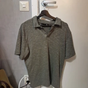 Olivgrön skjorta från 157, stl S - Olivgrön kortärmad skjorta i mjukt material från 157 med klassisk krage och två knappar framtill. Skjortan är kortärmad och har en enkel, stilren look som passar perfekt till jeans eller shorts. Materialet känns mjukt och bekvämt mot huden.