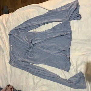 Ljusblå omlottopp från Design by Si - Supersöt ljusblå omlottopp från Design by Si i mjukt och tunt material. Toppen har långa ärmar med lätt utsvängda ärmslut och knytning framtill som ger en snygg och avslappnad look. Perfekt att styla med jeans eller kjol för en trendig vibe.