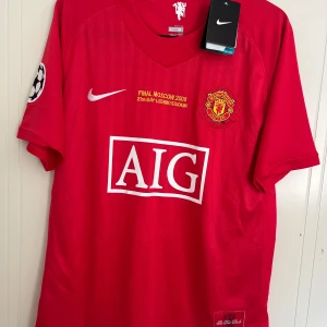 Manchester United 2007/2008 Hemmatröja  - Manchester Uniteds officiella matchtröja från Champions League-finalen i Moskva 2008. Röd med broderat klubbmärke, AIG-logga, Nike Swoosh och Champions League-patch på ärmen. Tillverkad i lätt Dri-FIT-material som andas. Snygg och ikonisk design för alla United-fans.