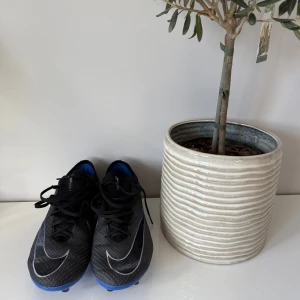 Nike Mercurial Vapor fotbollsskor svart/blå - Säljer ett par Nike Mercurial Vapor fotbollsskor i svart med blå detaljer och vita Nike-swooshes. Skorna har snörning, platt sula med dobbar och är tillverkade i syntetmaterial med Flyknit-teknologi för extra komfort och passform. Helt nya använda 1 träning. Ingen skada alls på sig. 