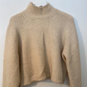 Beige stickad tröja med krage  - Mysig beige stickad polotröja med hög krage och långa ärmar. Kortare passform som passar bra till byxor med högre midja.