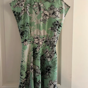 Mintgrön blommig klänning Zara Trafaluc - Superfin mintgrön klänning från Zara Trafaluc med svartvitt blommönster och tropiska detaljer. Modellen är kortärmad med markerad midja och lätt utställd kjol. Perfekt för sommarens alla tillfällen och riktigt skön att bära.