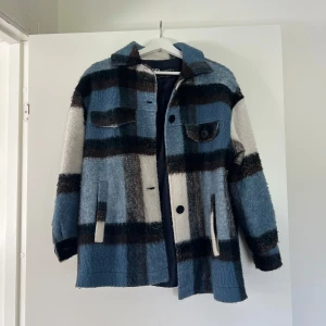 Rutig oversized jacka från Zara  - Snygg och trendig jacka från Zara i blå, svart och vit rutig design. Jackan har stora knappar framtill, två illustrerade bröstfickor med lock och en mjuk, ullig känsla. Perfekt för lager-på-lager och chill stil under höst och vår.