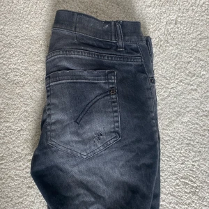 Dondup jeans  - Säljer ett par svarta slim fit jeans med snygga slitningar på benen och bakfickan. Jeansen har klassisk femficksdesign, smal passform och är tillverkade i stretchigt denim för extra komfort. Perfekta för dig som gillar en edgy och modern stil.