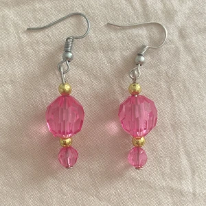 Rosa glittriga örhängen med pärlor - Säljer ett par snygga örhängen med facetterade rosa pärlor och små guldfärgade detaljer. De har en glittrig känsla och hängande design som ger extra färg till din look. Perfekta för dig som gillar att sticka ut med accessoarer!
