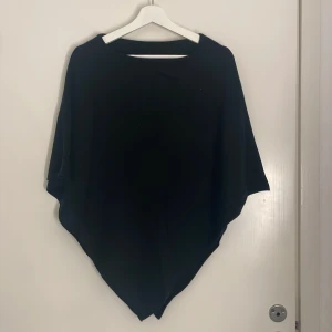 Svart poncho topp - En svart poncho med asymmetrisk nederkant från Glitter. Perfekt för lager-på-lager och ger en chill, avslappnad vibe. Toppens enkla design gör den lätt att matcha med olika outfits. (Aldrig använd)