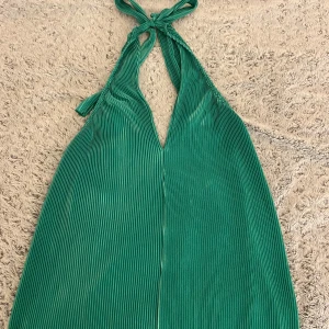 Grön plisserad halterneckklänning - Säljer denna klänning, aldrig använd🤗 Jätte fin färg och den går att knyta runt halsen. Klänningen går nästan till knäna