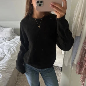 Svart stickad tröja - Mysig svart stickad tröja med rund halsringning och långa ärmar. Tröjan har en fluffig och mjuk känsla, perfekt för kyliga dagar. Enkel och stilren design som är lätt att matcha med jeans eller kjol.