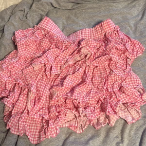 Rutig rosa volangkjol - Supersöt kort volangkjol i rosa och vitt rutigt tyg. Kjolen har flera lager med volanger som ger en fluffig och lekfull look. Perfekt för dig som gillar en gullig och trendig stil. Resår i midjan för extra komfort. Har sytt den själv! Passar mellan 32-38
