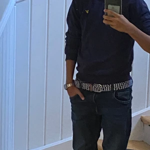 Mörkblå tröja från Lyle & Scott - Säljer en mörkblå långärmad tröja från Lyle & Scott med klassisk v-ringning och gul logga på bröstet. Tröjan är i mjuk bomull och har ribbade muddar vid ärmslut och nederkant. Perfekt för en stilren och avslappnad look.