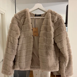 Beige pälsjacka från Gina Tricot - Supermjuk och fluffig beige pälsjacka från Gina Tricot. Jackan har lång ärm, rak passform och är fodrad på insidan. Perfekt för dig som vill ha en mysig och trendig look under kyliga dagar.