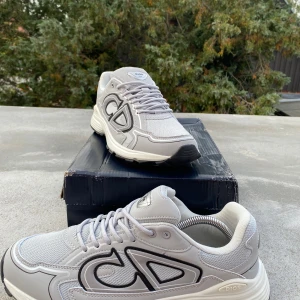 Grå  sneakers med CD-logga - Snygga grå sneakers med stor CD-logga på sidan och detaljer i svart och vitt. Skorna har en chunky vit sula med svarta partier undertill och är tillverkade i mesh och syntetmaterial. Perfekta för dig som gillar exklusiva och trendiga sneakers. Boxen är sönder därför så lågt pris (A-cop)