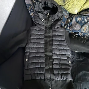 Svart moncler cardigan  - Säljer en svart pufferjacka från Moncler med huva och ribbade ärmar. Jackan har quiltad framsida, dragkedja, fickor med tryckknappar och en extra ficka med dragkedja på ärmen. Perfekt för kalla dagar och riktigt snygg streetstil.