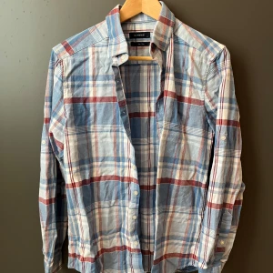 Rutig skjorta från LC Waikiki, slim fit - Säljer en snygg rutig skjorta från LC Waikiki i slim fit. Skjortan har blå, röda och vita rutor, klassisk krage och knäppning framtill. Perfekt för dig som gillar en stilren och avslappnad look. Tillverkad i mjuk bomull och har långa ärmar.