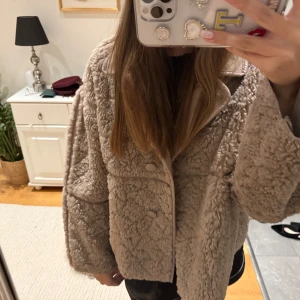 Beige teddyjacka med knappar - Supermysig beige teddyjacka med oversized passform och stora knappar framtill. Jackan har bred krage och är tillverkad i fluffigt teddy-material som håller dig varm och ger en chill vibe. Perfekt att slänga på sig över en hoodie eller t-shirt.