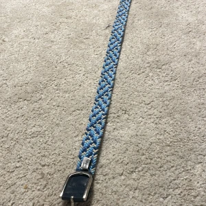 Blått flätat bälte från Onewear - Snyggt flätat bälte från Onewear Sweden i olika blå nyanser, vitt och beige. Bältet har ett coolt mönster och detaljer i mörkblått skinn vid spännet. Perfekt accessoar för att lyfta din outfit med lite färg och stil. 70cm