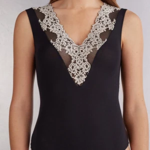Spets body - Supersnygg svart ärmlös linne med djup v-ringning och vit spets upptill. Spetsen har blommigt mönster och ger en elegant touch. Perfekt att styla med jeans eller kjol för en trendig look.
