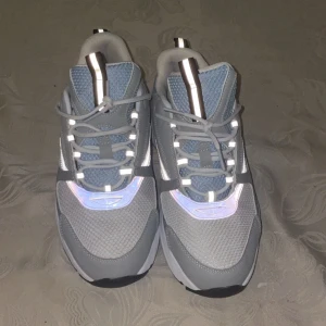 B22 blå/vit pris kan diskuteras - Snygga  sneakers i grått och ljusblått med reflekterande detaljer. Ovandelen är i mesh och syntet, med coola silvriga inslag på plösen och snörning framtill. Sulan är tjock och ger en sportig vibe, perfekt för dig som gillar streetstyle. Utan box 