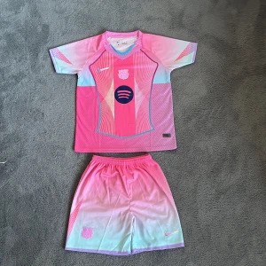 Barça nya Rosa kit (REP) - Säljer ett Barcelona fotbollströja  Nike i Dri-Fit material. Tröjan är kortärmad med coolt grafiskt mönster i rosa, lila och turkos, samt klubbmärke och Spotify-logga på bröstet. Shortsen har matchande färgskiftning och elastisk midja. Perfekt för dig som vill sticka ut på planen.