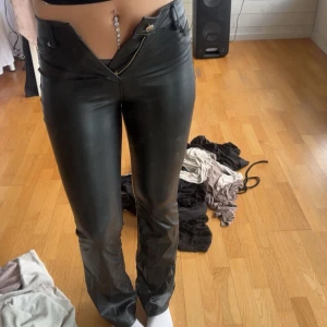 Svarta skinnbyxor med rak passform - Säljer ett par svarta byxor i skinnimitation med rak passform och låg midja. Byxorna har klassiska fickor fram och bak samt dragkedja och knapp i midjan. Perfekta för en edgy look och passar till crop tops eller oversized tröjor.