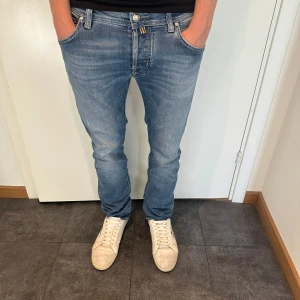 Jacob Cohen 622 - Säljer ett par snygga Jacob Cohen jeans i ljusblå tvätt med klassisk femficksdesign. Jeansen har normal passform, raka ben och subtila slitningar för en avslappnad look. Tillverkade i mjuk bomullsdenim med lite stretch för extra komfort. Modellen är 176 och väger 65kg.