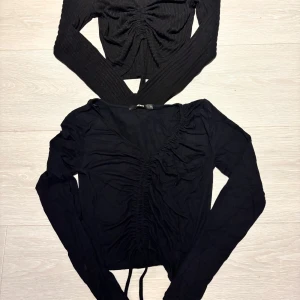 Svarta långärmade toppar med snörning - Två svarta långärmade toppar med snörning framtill. Ena toppen är ribbad och croppad, medan den andra har v-ringning och dragsko längs magen. Från Bik Bok och New Yorker