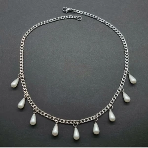 Silverhalsband med droppformade pärlor - Stilrent halsband i silverfärgad metall med kedja och sju hängande droppformade vita pärlor. Perfekt för dig som gillar en cool och elegant vibe. Kedjan har ett klassiskt lås och pärlorna ger en unik touch till din look.