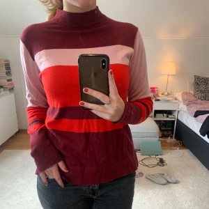 Randig polotröja från KappAhl - Säljer en snygg polotröja från KappAhl i storlek S. Tröjan har breda ränder i vinrött, rosa och rött, med hög krage och långa ärmar. 