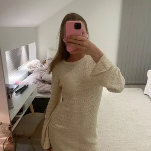 Stickad beige kortklänning - Superfin stickad kortklänning i beige med långärmade trumpetärmar och rund hals. 