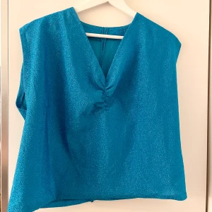 Glittrig blå topp  - Snygg och festlig blå topp med v-ringning och lätt rynk framtill, ganska lös passform, saknar etikett men den känns som mellan M och L💙 Mycket bra skick, saknar etikett så vet inte märket. Kolla gärna in mina andra annonser, försöker bli av med allt så snart som möjligt 💝pris alltid förhandlingsbart, brukar gå med på de flesta prisförslag!😚 säljer mycket äkta vintage! 💝