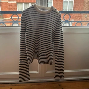 Randig stickad tröja Zadig & Voltaire - Snygg stickad tröja från Zadig & Voltaire med svartvita ränder och coola knappar på ena axeln. Tröjan har lång ärm och rund halsringning, perfekt för dig som gillar en klassisk men trendig look.