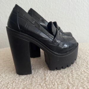 Nya. Svarta chunky loafers med platå - Snygga svarta loafers med grov platåsula och hög klack. Skorna har ett glansigt, krokopräglat mönster och rund tå. Perfekta för dig som vill sticka ut med en edgy och trendig look. Nya, bara testade. Storlek 35, innelängd 22.5cm.