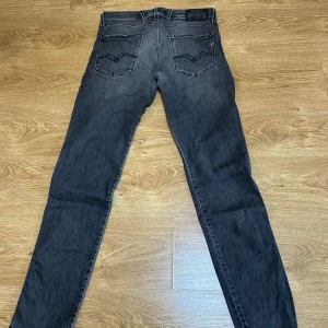 Replay Anbass slim fit svarta jeans - Säljer ett par Replay Anbass slim fit jeans i svart tvättad denim. Jeansen har klassisk femficksdesign, snygga detaljer på bakfickorna och en smal passform som sitter tajt längs benen. Perfekta för dig som gillar en modern och stilren look.