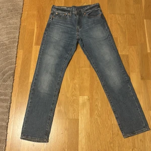 Levi's 501 blå jeans straight fit - Klassiska blå Levi's 501 jeans med rak passform och femficksdesign. Jeansen har en snygg mellanblå tvätt, knappgylf och ikonisk läderpatch bak i midjan. Perfekta till vardags för en avslappnad och tidlös look.