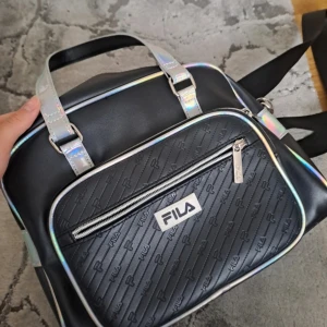 Svart axelväska från FILA  - Cool svart axelväska från FILA med holografiska handtag och detaljer. Väskan har ett stort huvudfack, ytterfack med dragkedja och präglad logga framtill. 